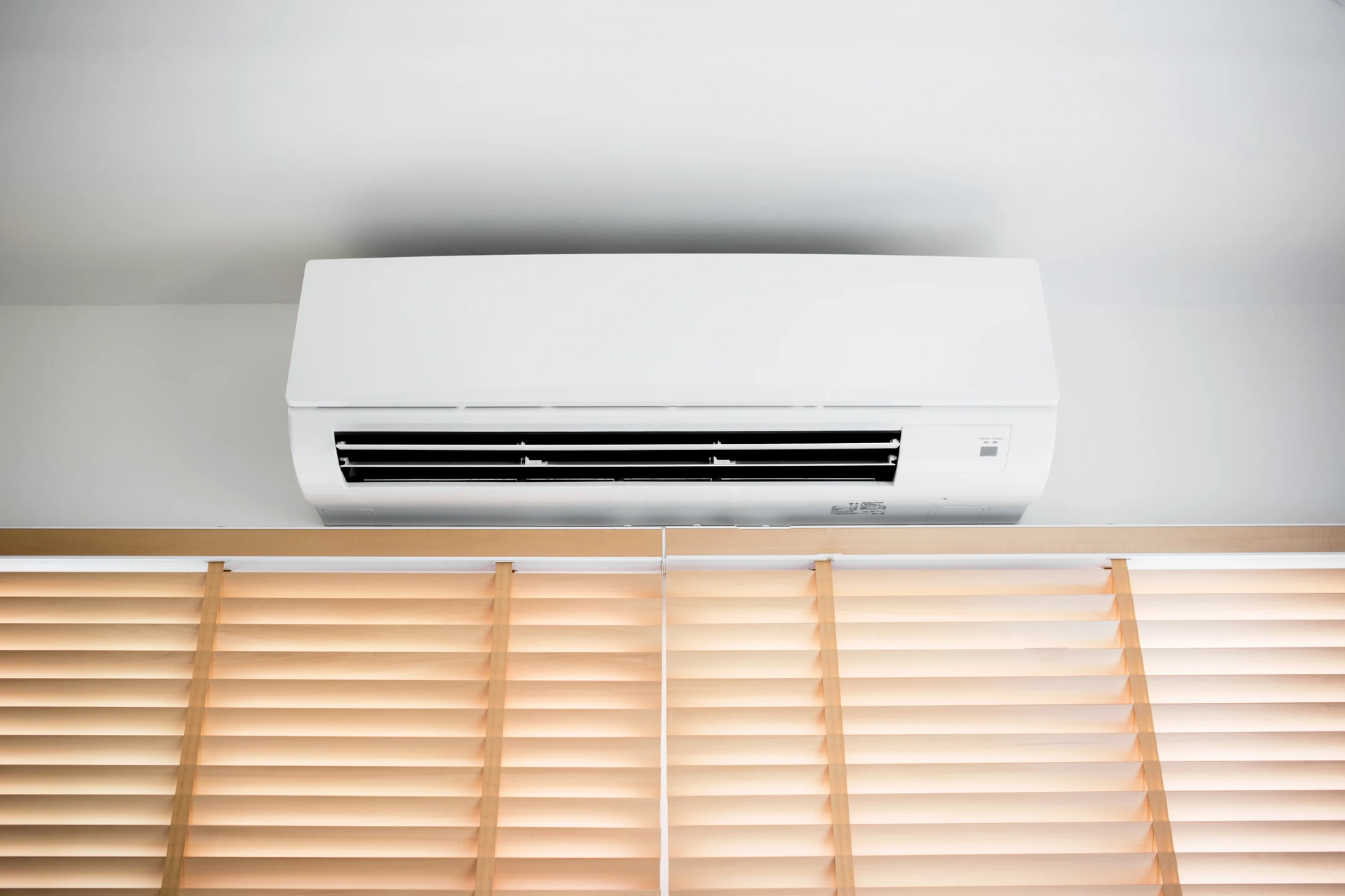Intérieur résidentiel moderne avec climatiseur split mural blanc installé au-dessus de stores vénitiens en bois