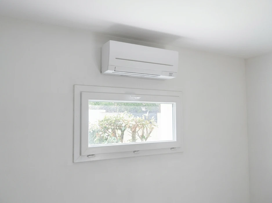 Intérieur épuré, mur blanc avec climatiseur mural gainable **Mitsubishi Electric** (unité intérieure split system, modèle MSZ) installé en hauteur