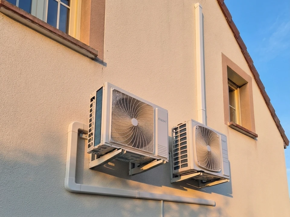 Jardin extérieur ensoleillé avec unité extérieure de pompe à chaleur air/air installée sur dalle béton contre mur enduit