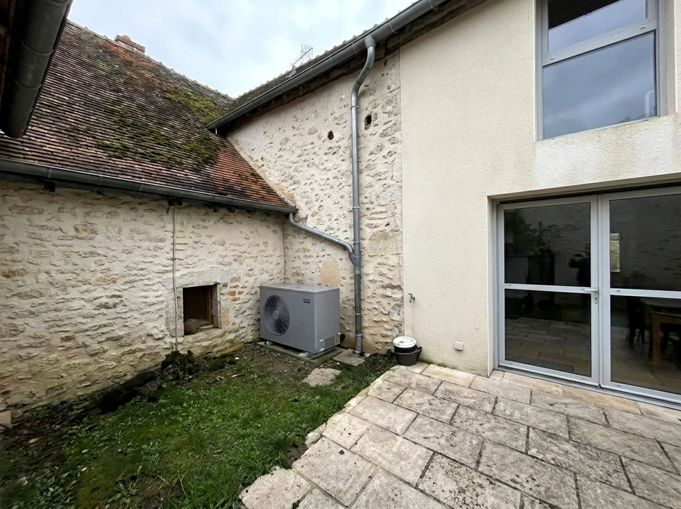 Jardin extérieur ensoleillé avec unité extérieure de pompe à chaleur air/air installée sur dalle béton contre mur enduit