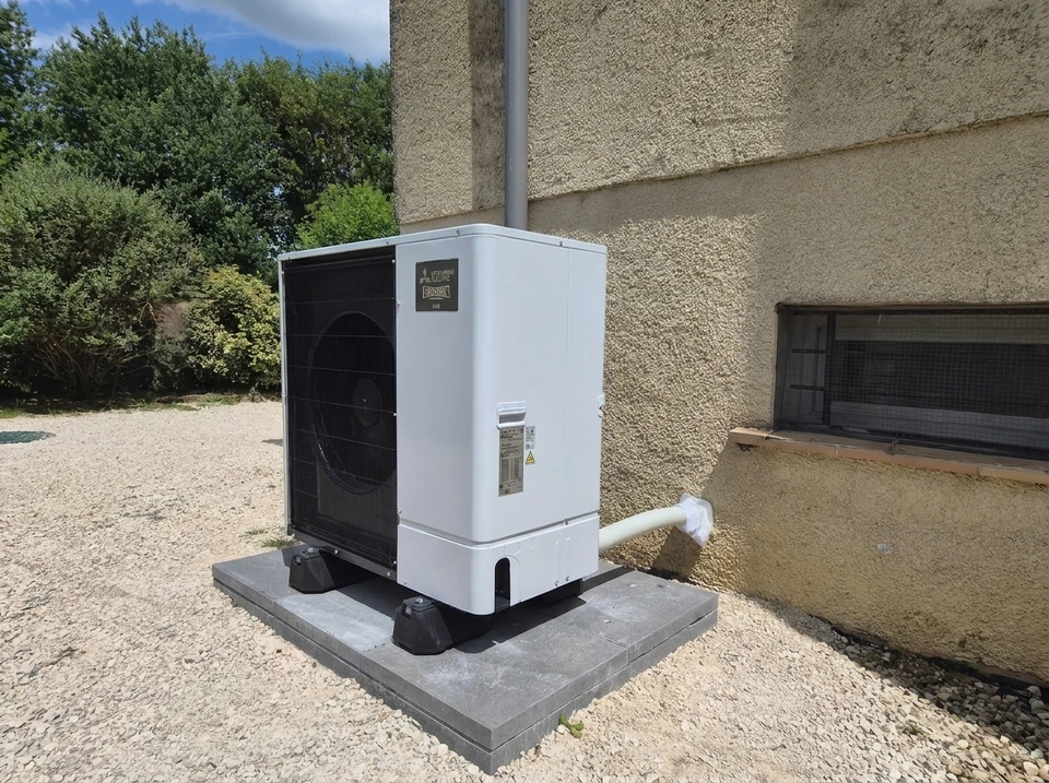 Extérieur résidentiel avec unité de climatisation installée sur socle béton contre mur beige