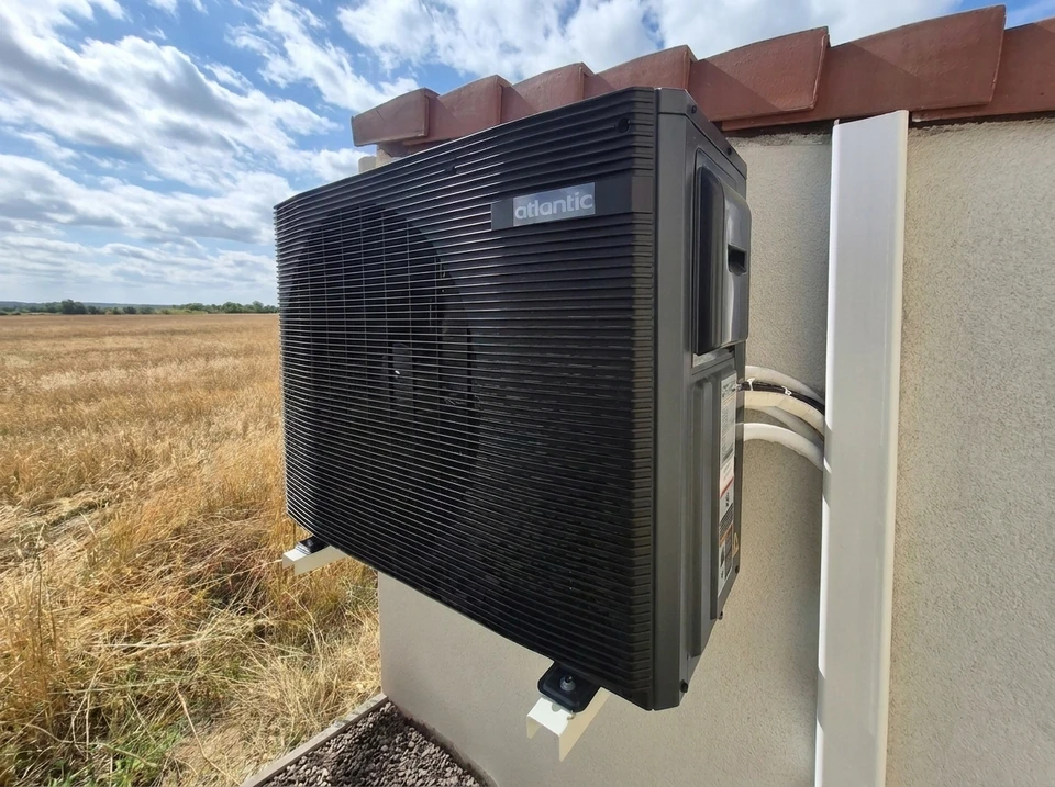 Jardin extérieur ensoleillé avec unité extérieure de pompe à chaleur air/air installée sur dalle béton contre mur enduit